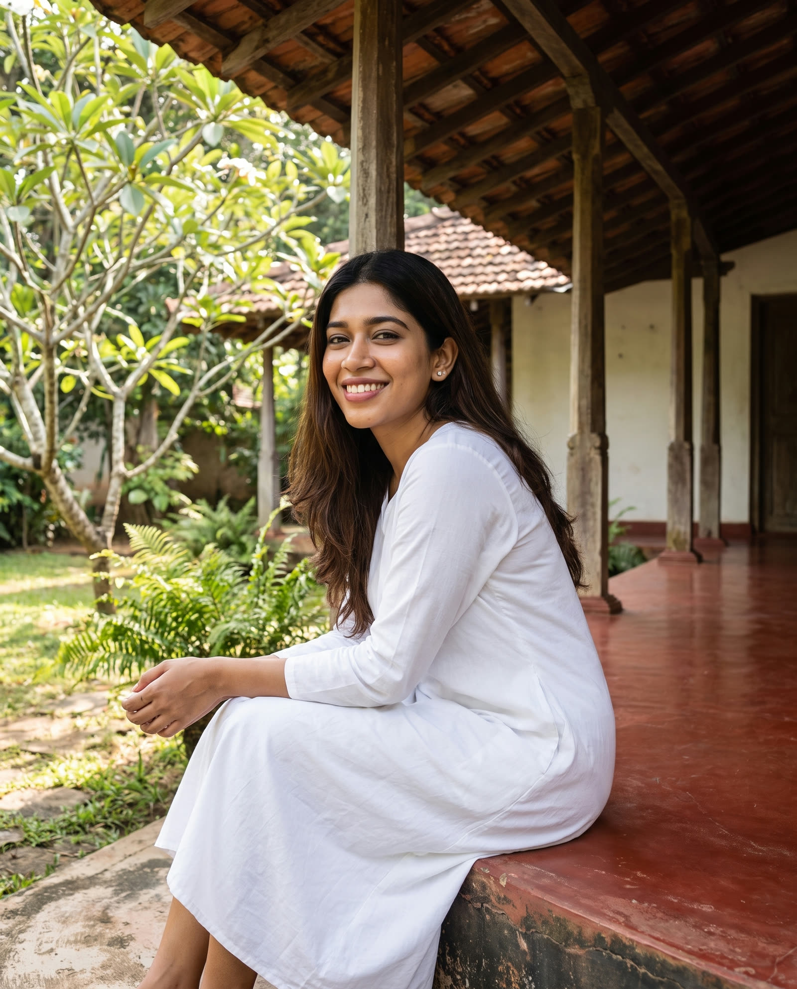 Jayani Perera in white, sitting on the edge of an old Sri Lankan verandah with frangipani behind her, smiling